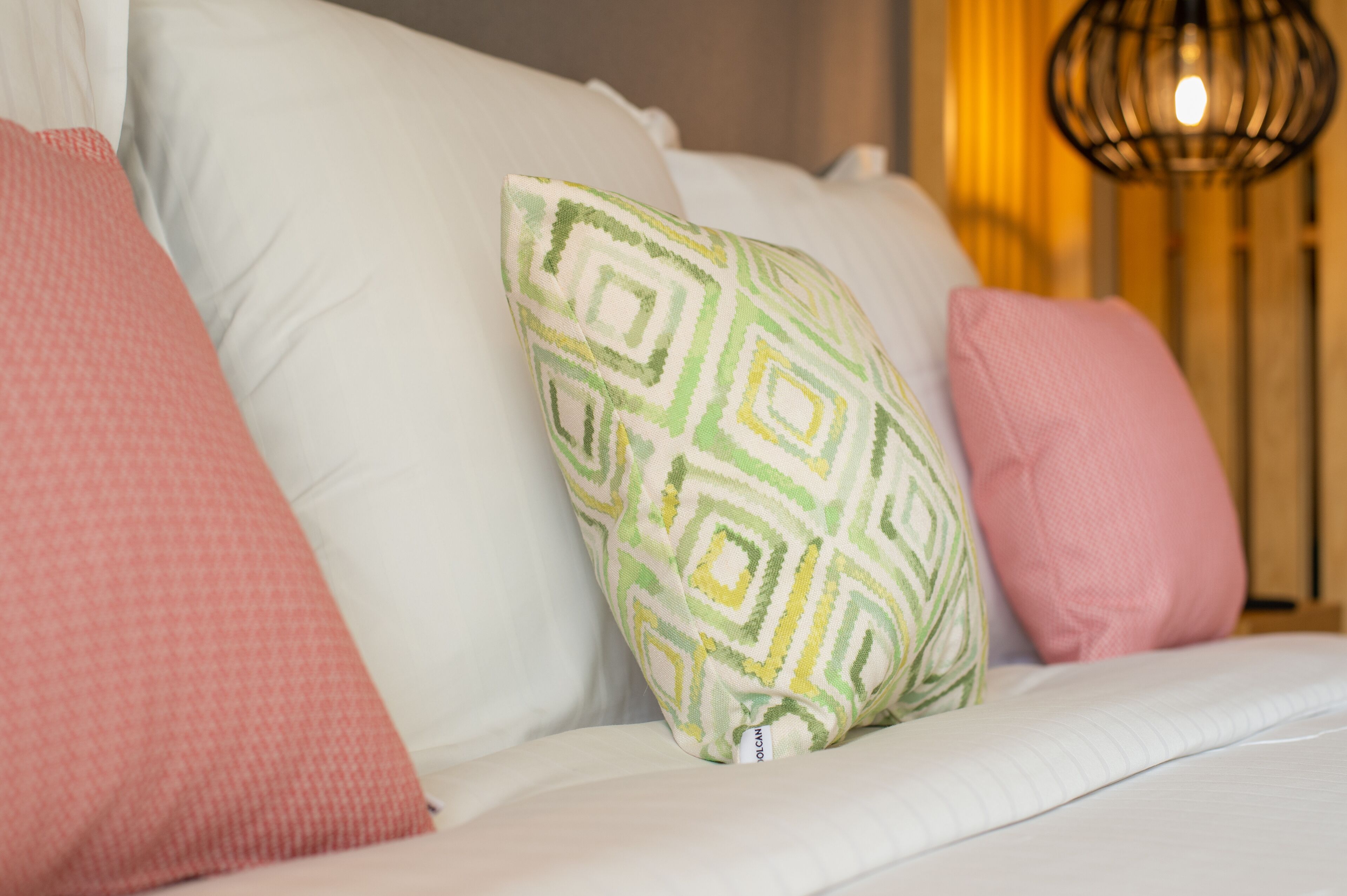 A bed with white bedding and multiple pillows, including a green and yellow patterned pillow.