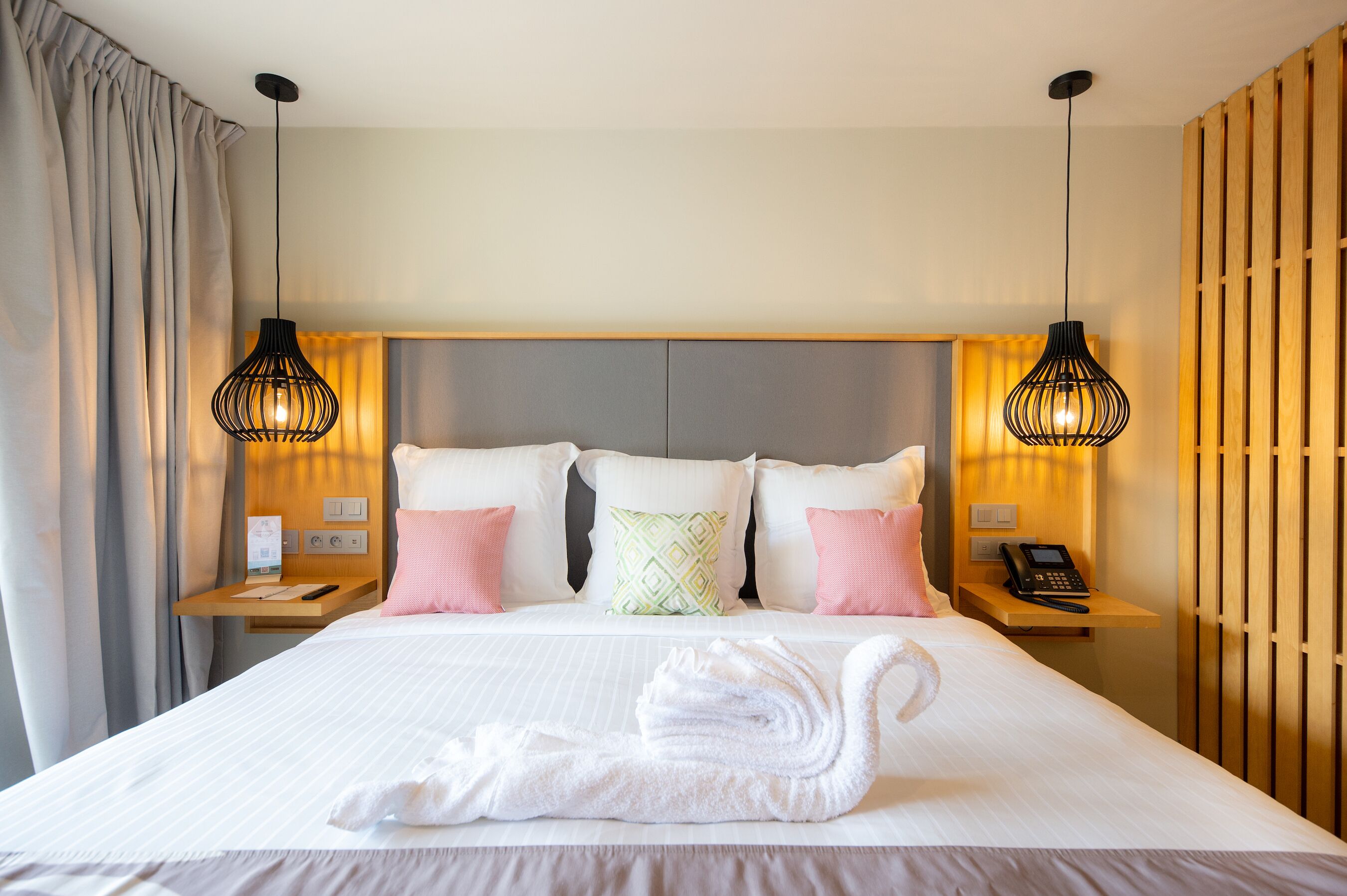 A hotel room with a neatly made bed, two bedside tables with lamps, a phone, and a wooden panel wall.