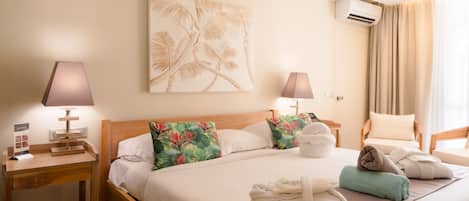 A hotel room with a bed, two bedside tables, a wall-mounted air conditioner, and a window with curtains.
