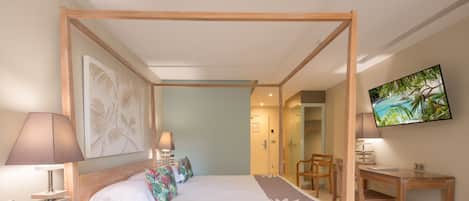 Una cama con dosel de madera, un escritorio con lámpara, un teléfono y un televisor en la pared.