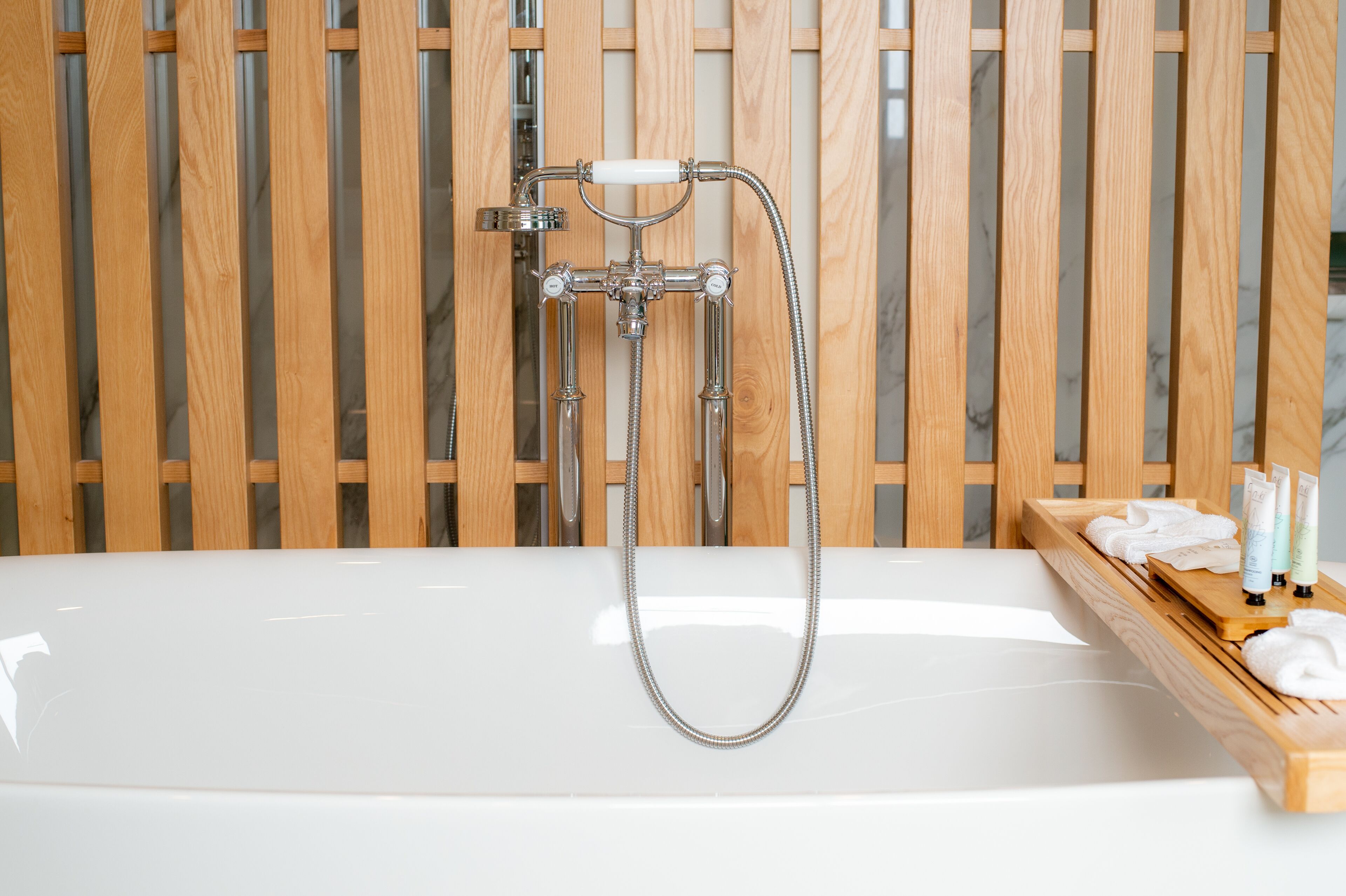 A bathtub with a showerhead and a wooden shelf with toiletries.