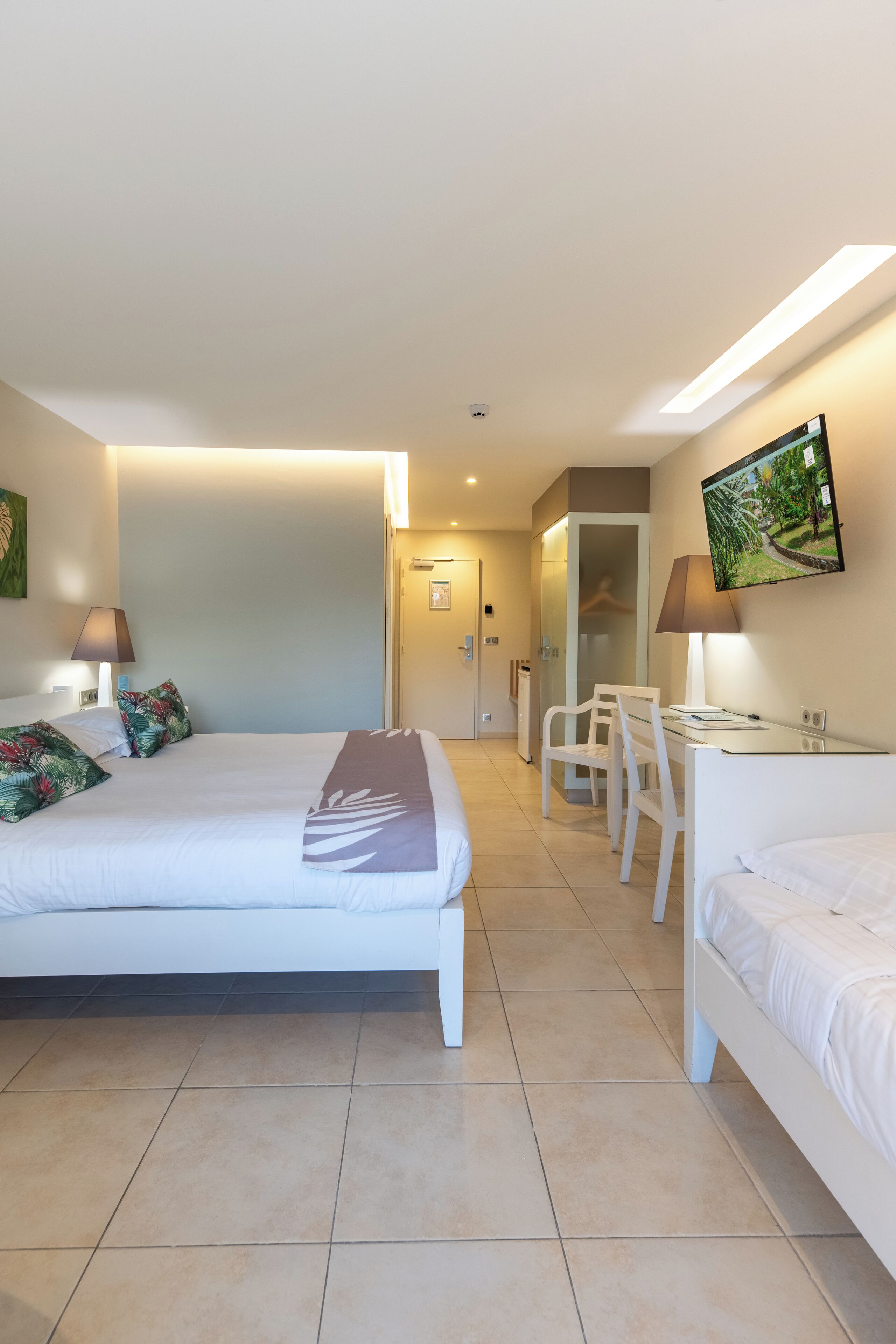 A hotel room with a large bed, a desk, and a chair. There is a TV mounted on the wall and a door leading to a bathroom.