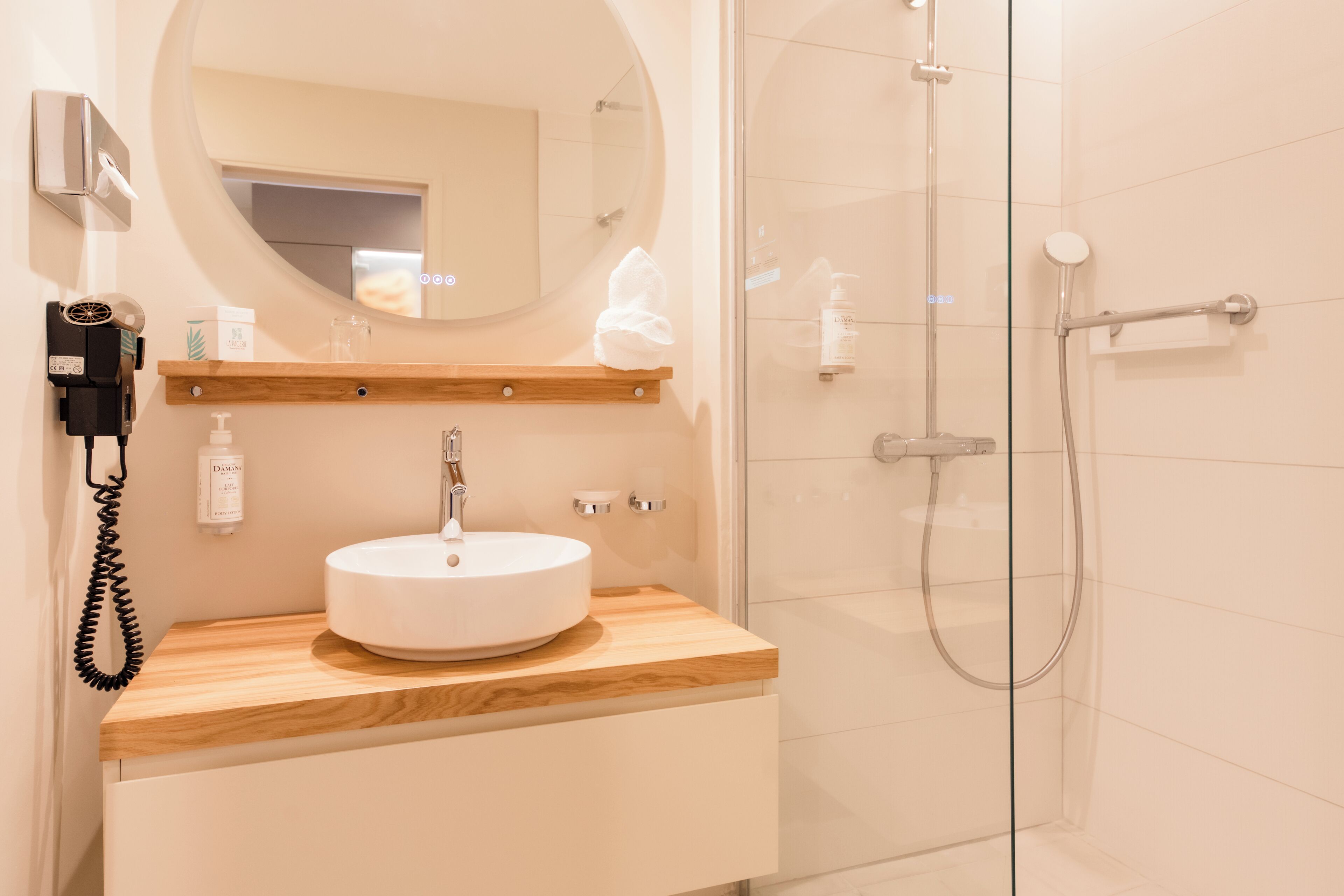 A modern bathroom with a round mirror, wooden vanity, white sink, and glass shower enclosure.