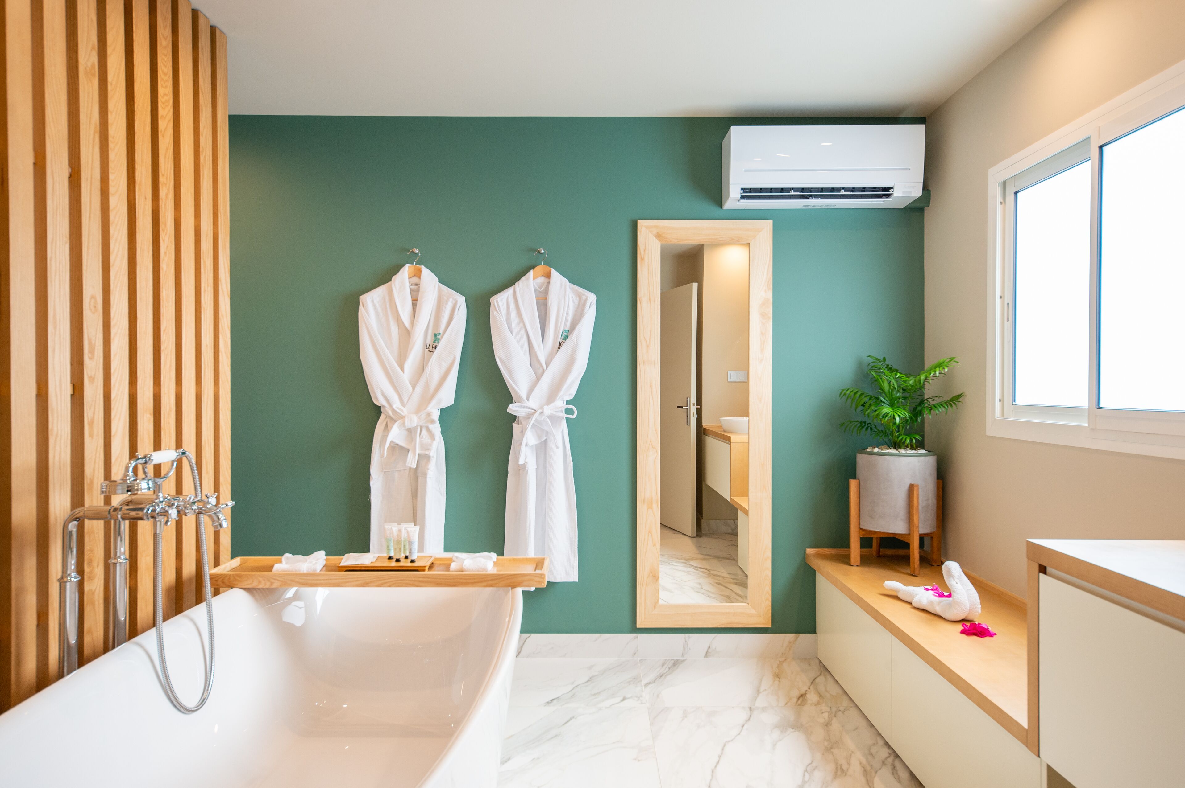 Un baño moderno con una bañera independiente, paneles de madera, un espejo y una planta en maceta.