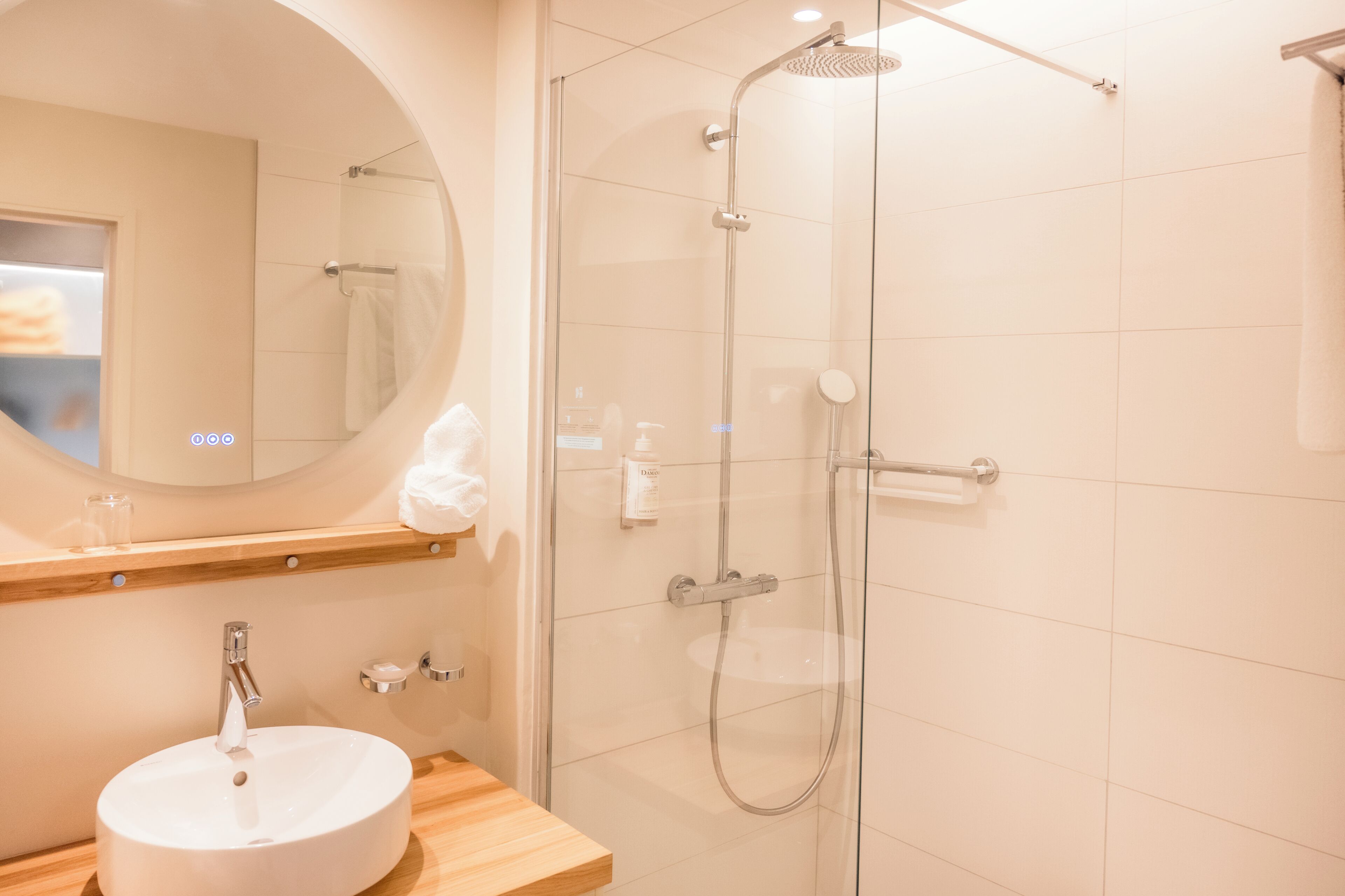 Un baño moderno con un espejo redondo, un lavamanos y una zona de ducha con mampara de vidrio.