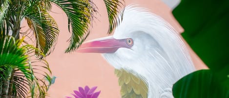 A mural of a white bird holding a purple flower, surrounded by green foliage.