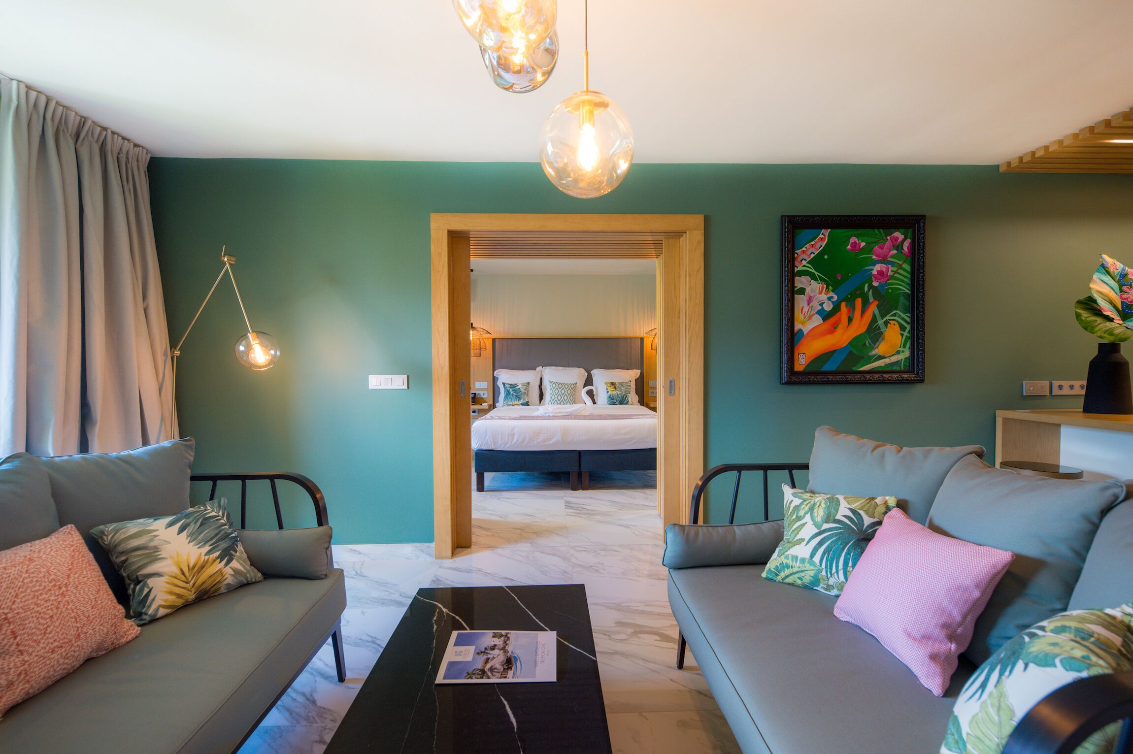 A modern hotel room with a large bed, two sofas, a coffee table, and a painting on the wall.