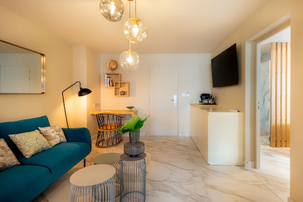 A modern living room with a blue sofa, a coffee table, and a TV mounted on the wall. - Hotel La Pagerie (Trois-Ilets)