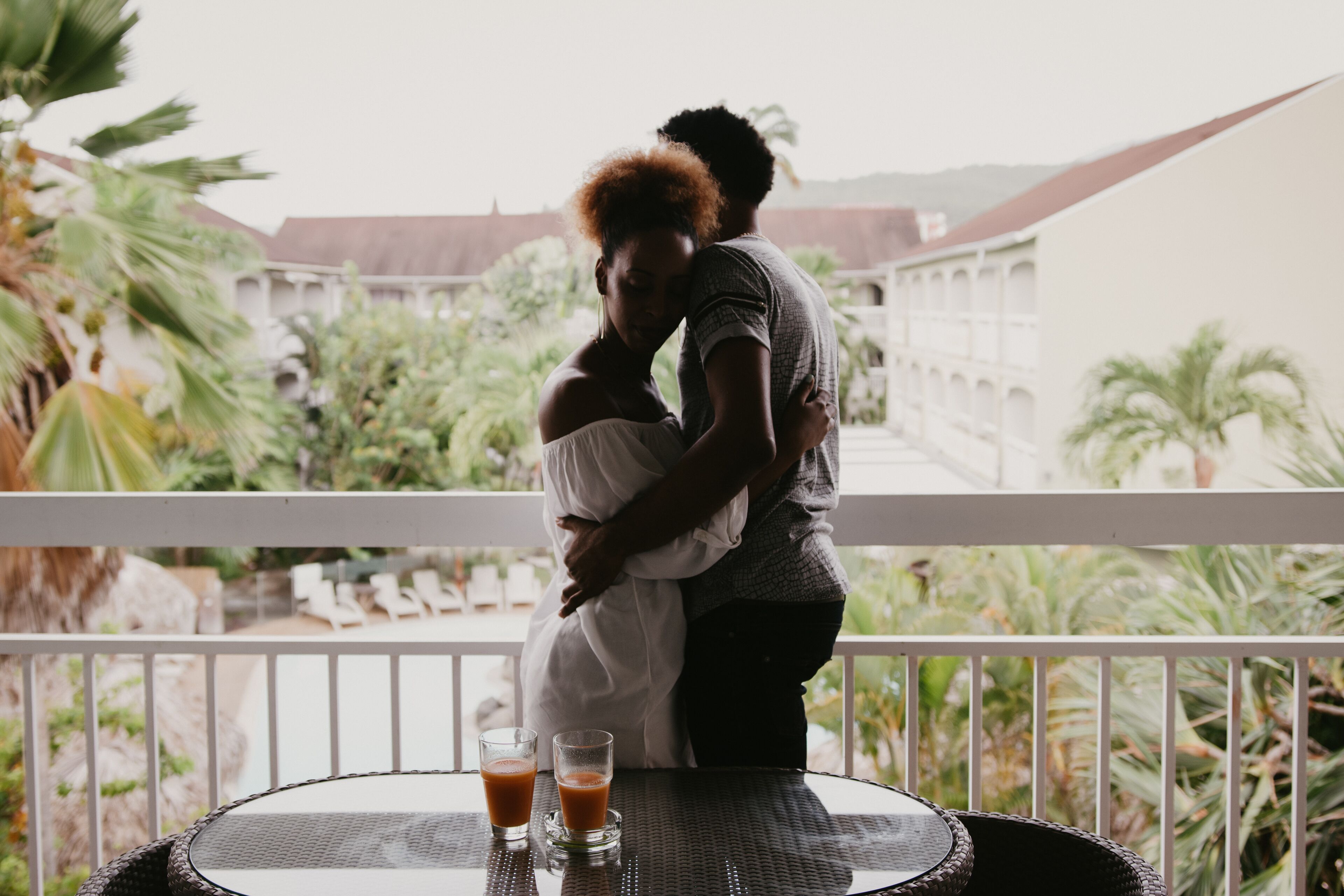 A couple embracing on a balcony with a view of a building and palm trees.