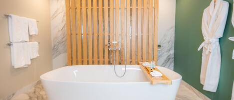 Un baño moderno con una bañera independiente, listones de madera, paredes de mármol y toallas blancas.
