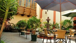An outdoor patio with wicker chairs, a large umbrella, and potted plants. - Hotel El Ducado (Lima)
