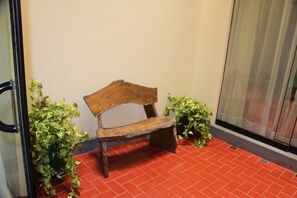 Un banc en bois au design rustique, placé sur un sol carrelé de tuiles rouges, et bordé de plantes en pot.