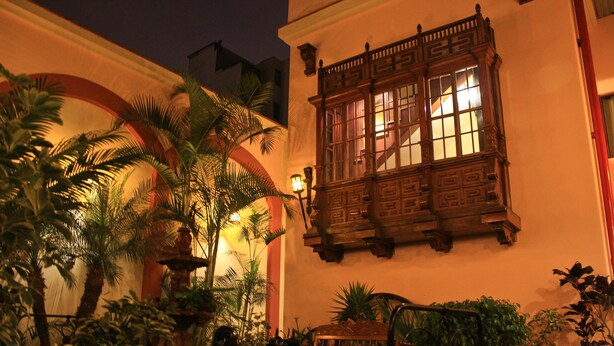 A courtyard with a wooden bench, palm trees, and a fountain. - Hotel El Ducado (Lima)