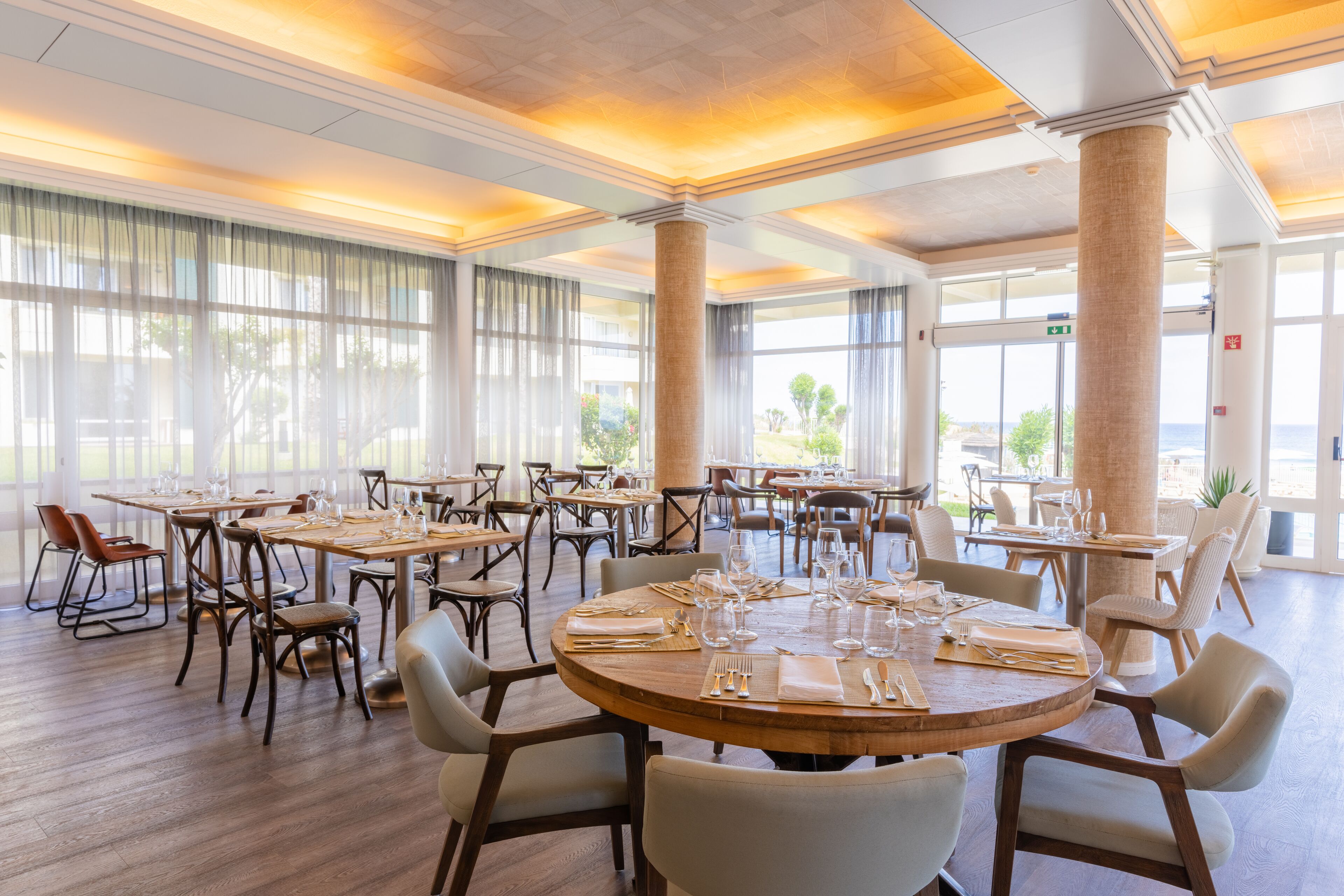 Un vaste espace dédié à la salle à manger, avec de nombreuses tables et chaises, de grandes fenêtres et un plafond haut orné de colonnes.