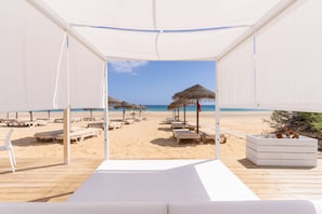 A beach view from a covered area with lounge chairs and a thatched umbrella. - Vila Baleira Suites (Porto Santo)