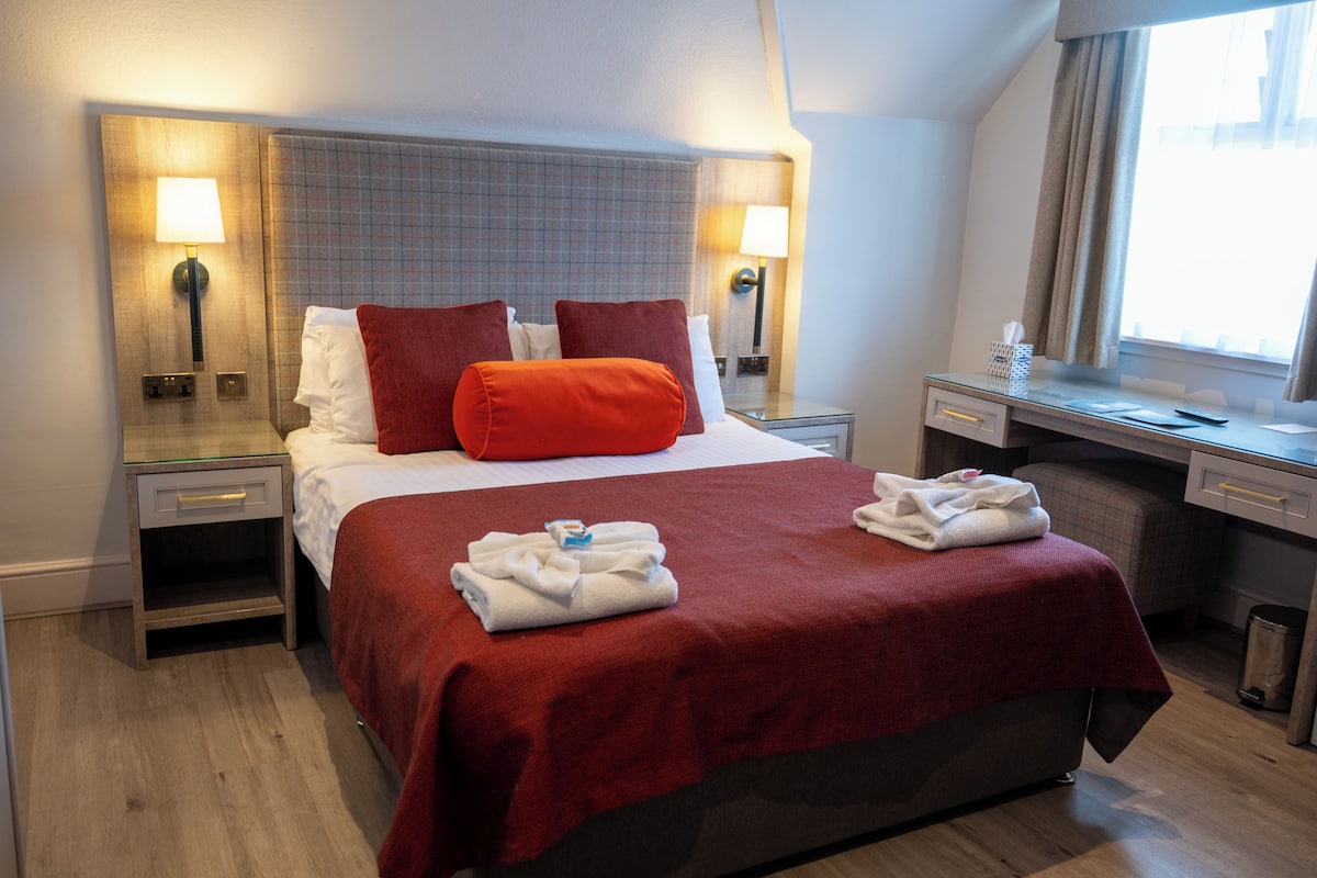Een hotelkamer met een bed, twee nachtkastjes, een bureau en een raam.