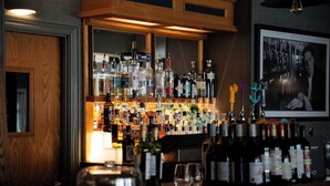 Un espace bar avec des étagères remplies de bouteilles d’alcool, de verres et un comptoir en bois.
