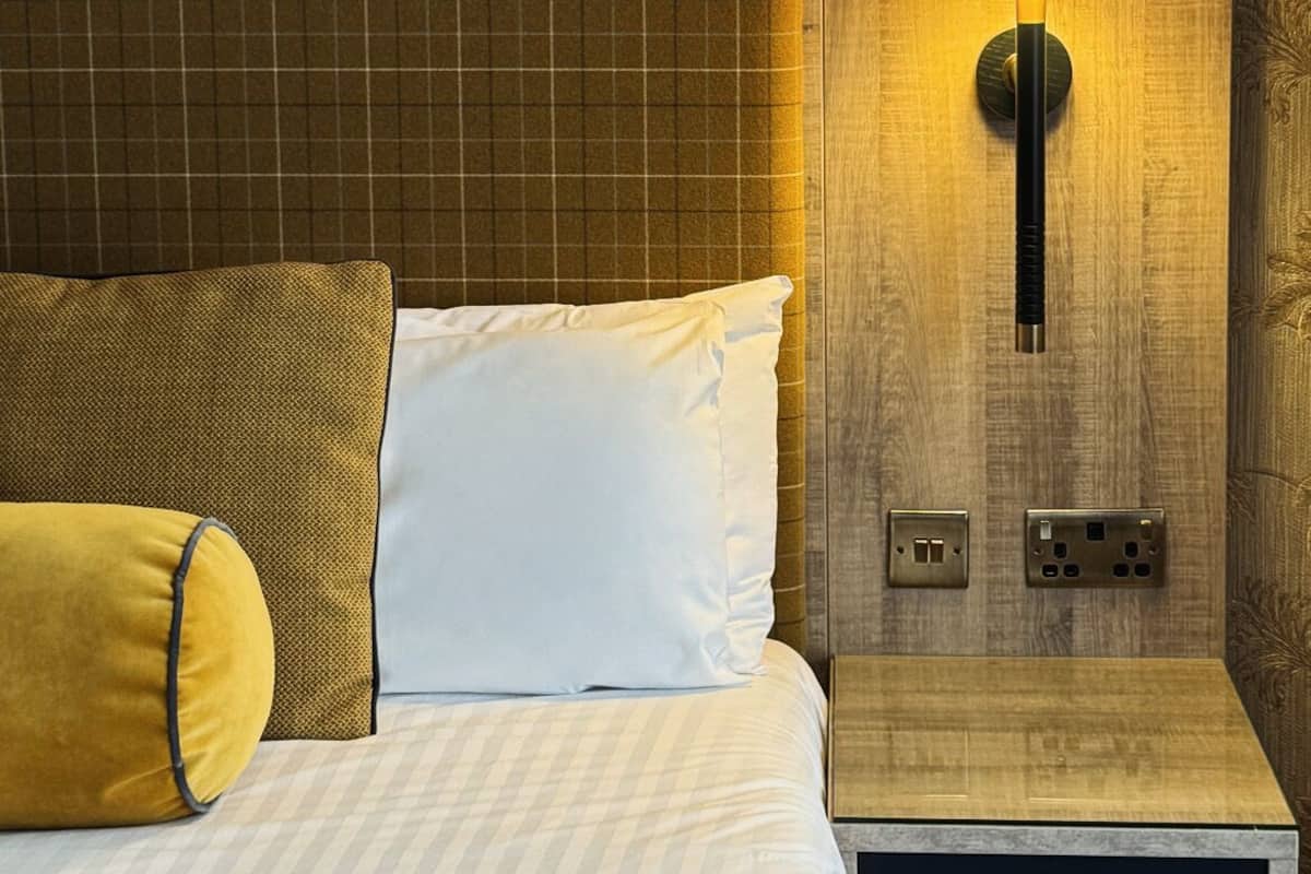 Een hotelkamer met een bed, nachtkastje, lamp en een muur met bloemenprint.