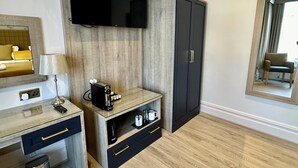 Une chambre d’hôtel moderne équipée d’un téléviseur à écran plat fixé au mur, d’un meuble en bois avec un miroir, d’un bureau avec une lampe et d’une machine à café.