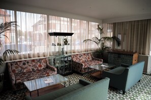 Un hall d’hôtel avec un canapé, des fauteuils, une vitrine et un sol à motifs.