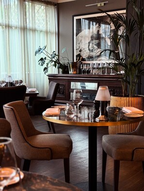 Een eethoek met een ronde tafel, stoelen en een bar met een grote spiegel en planten.