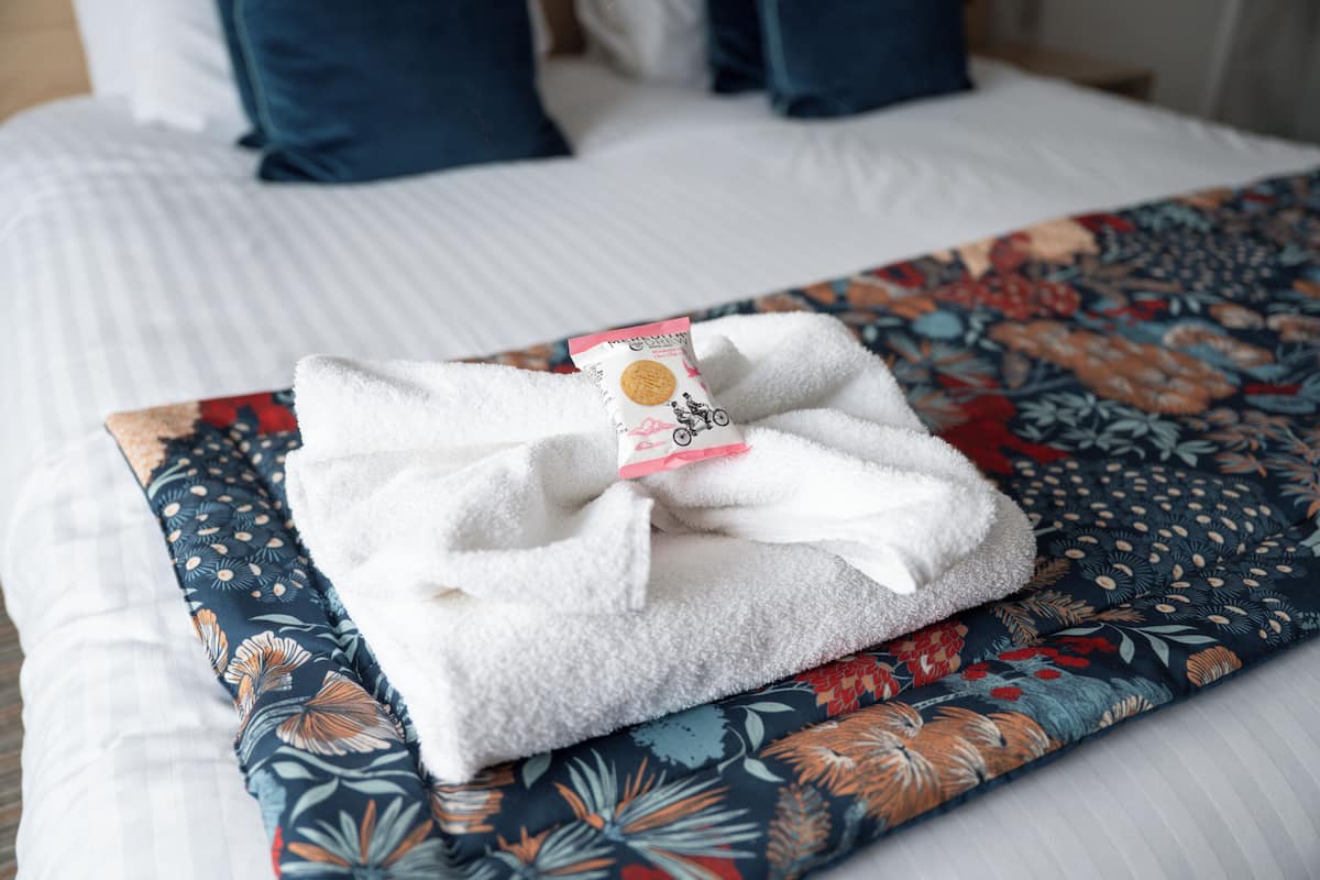 Een keurig gevouwen witte handdoek op een bed met een bloemenprint deken.