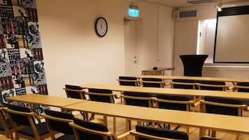 A classroom with rows of wooden desks and chairs, a clock on the wall, and a projector screen.