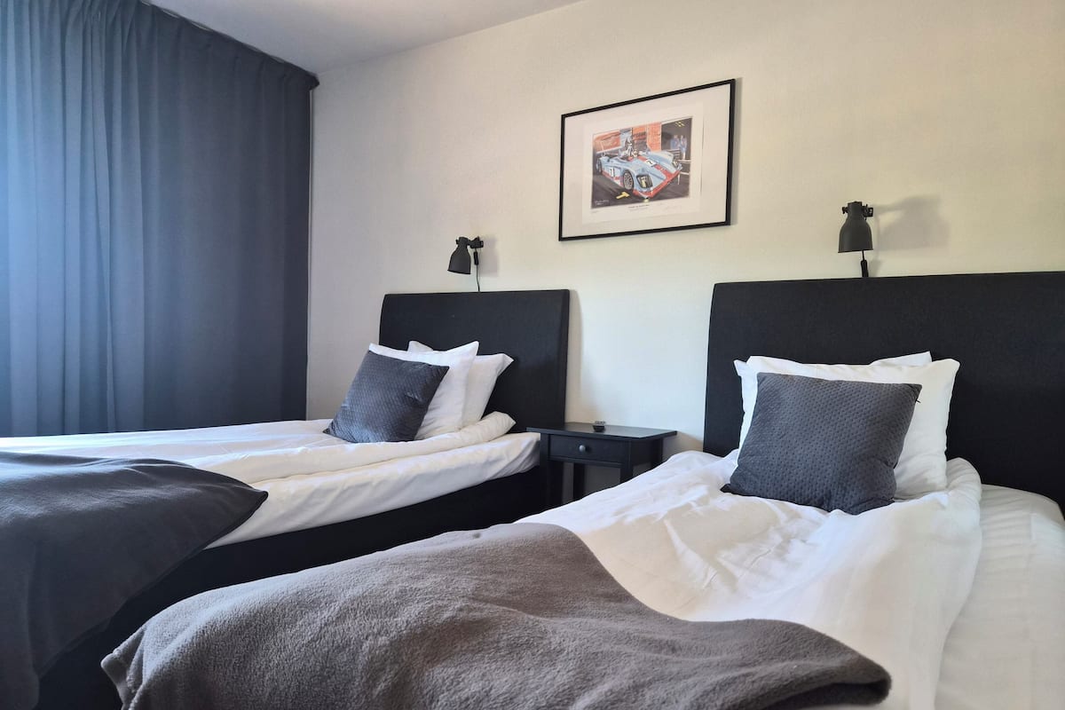 A hotel room with two beds, a nightstand, a lamp, a framed picture on the wall, and a window with curtains.