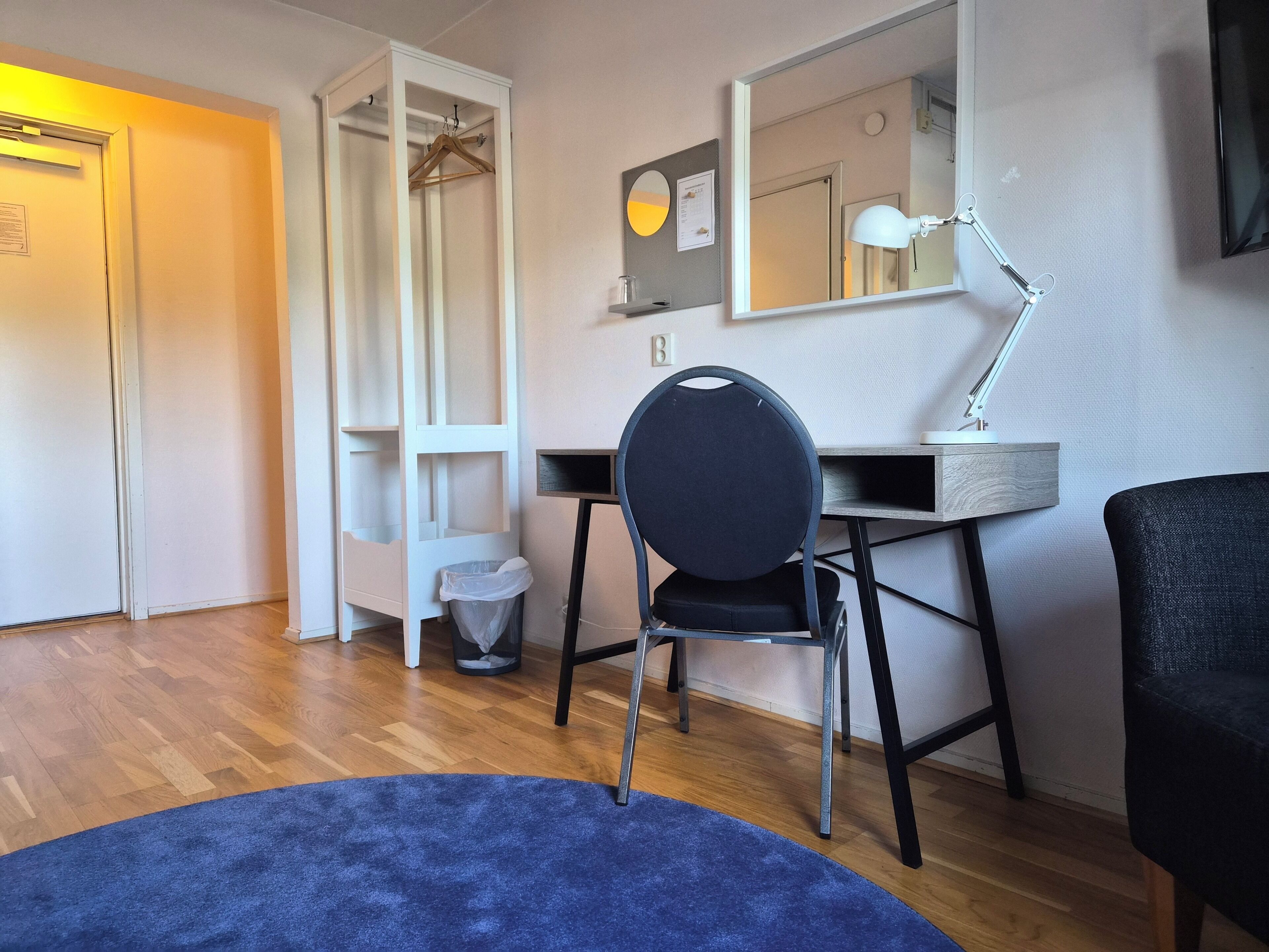 Una habitación con escritorio, silla, espejo y una alfombra azul.