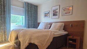 Un dormitorio con cama, mesita de noche, ventana con cortinas y tres cuadros en la pared.