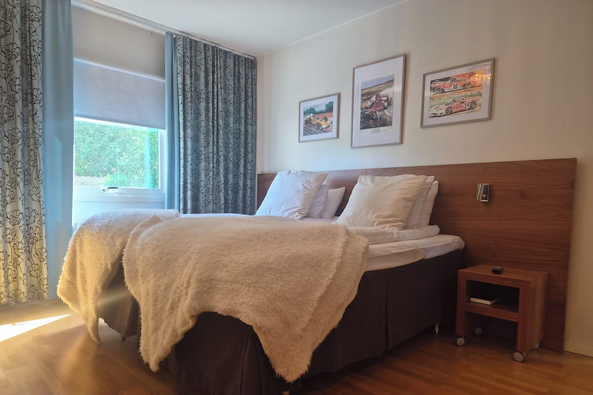 A bedroom with a bed, a nightstand, a window with curtains, and three framed pictures on the wall.