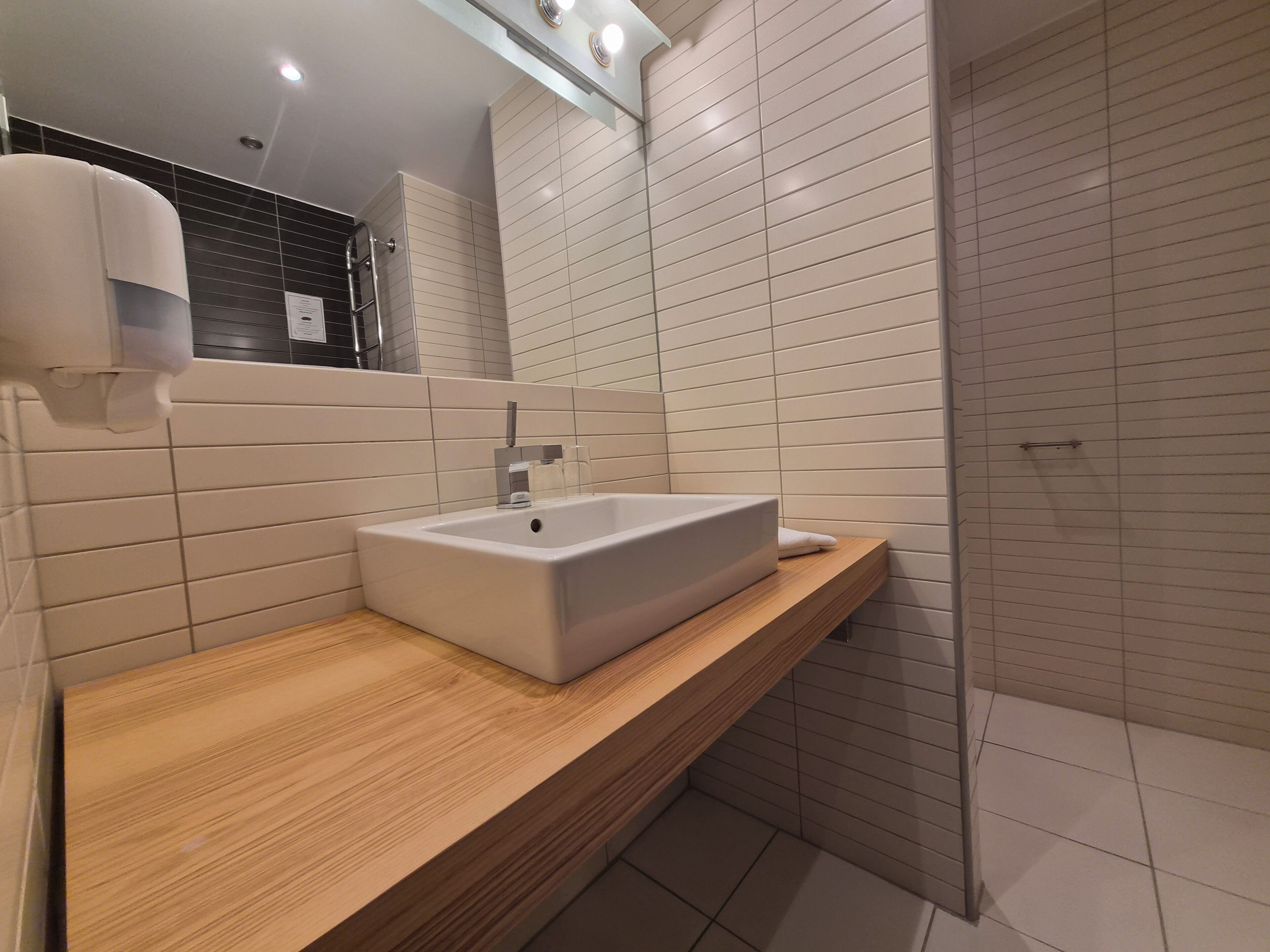 A modern bathroom with a rectangular sink, wooden countertop, and tiled walls.