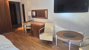 Una habitación moderna con un escritorio de madera, dos sillas, una mesa redonda, un televisor montado en la pared y un armario.