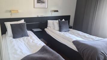 A hotel room with two single beds, a headboard, bedside tables, a wall-mounted light, and a framed picture.