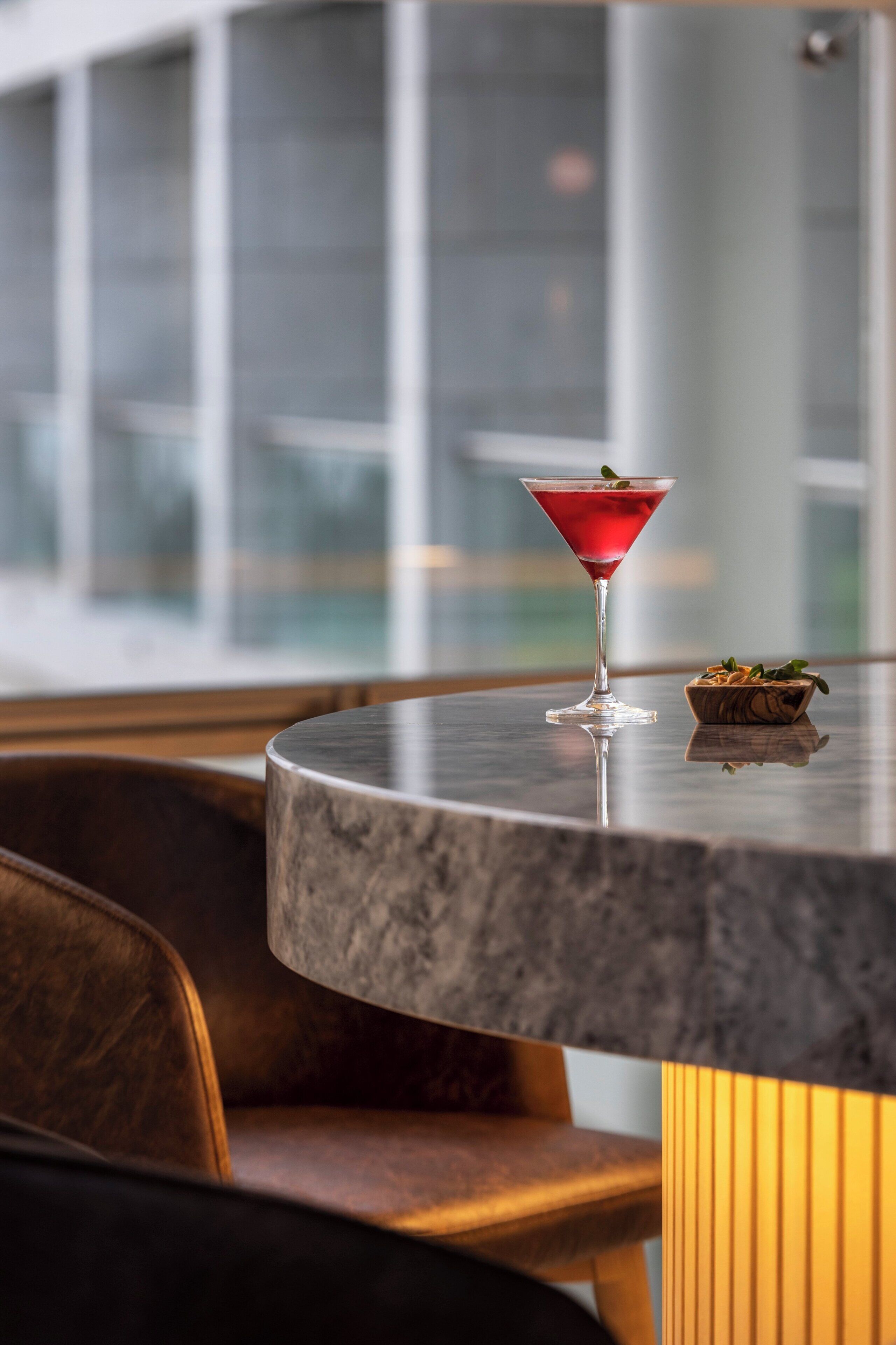 A bar area with a round marble table, a martini glass with a garnish, and a small bowl of nuts on the table.