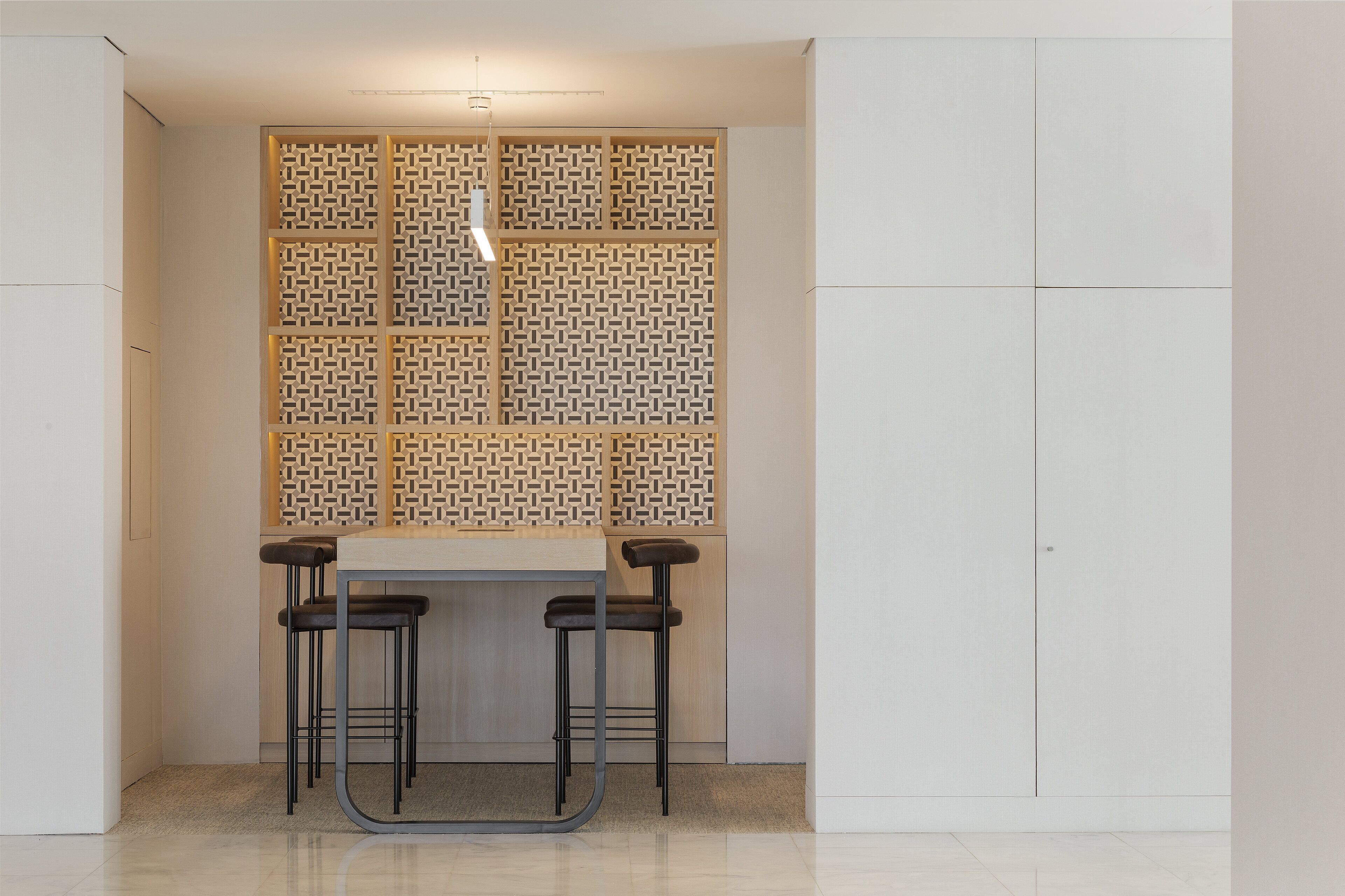 A modern kitchen with a central island, two bar stools, and a decorative panel with a geometric pattern.