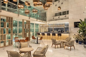 A spacious lobby with a bar area, seating arrangements, and a view of the outside through large windows. - Crowne Plaza Caparica Lisbon by IHG (Almada)