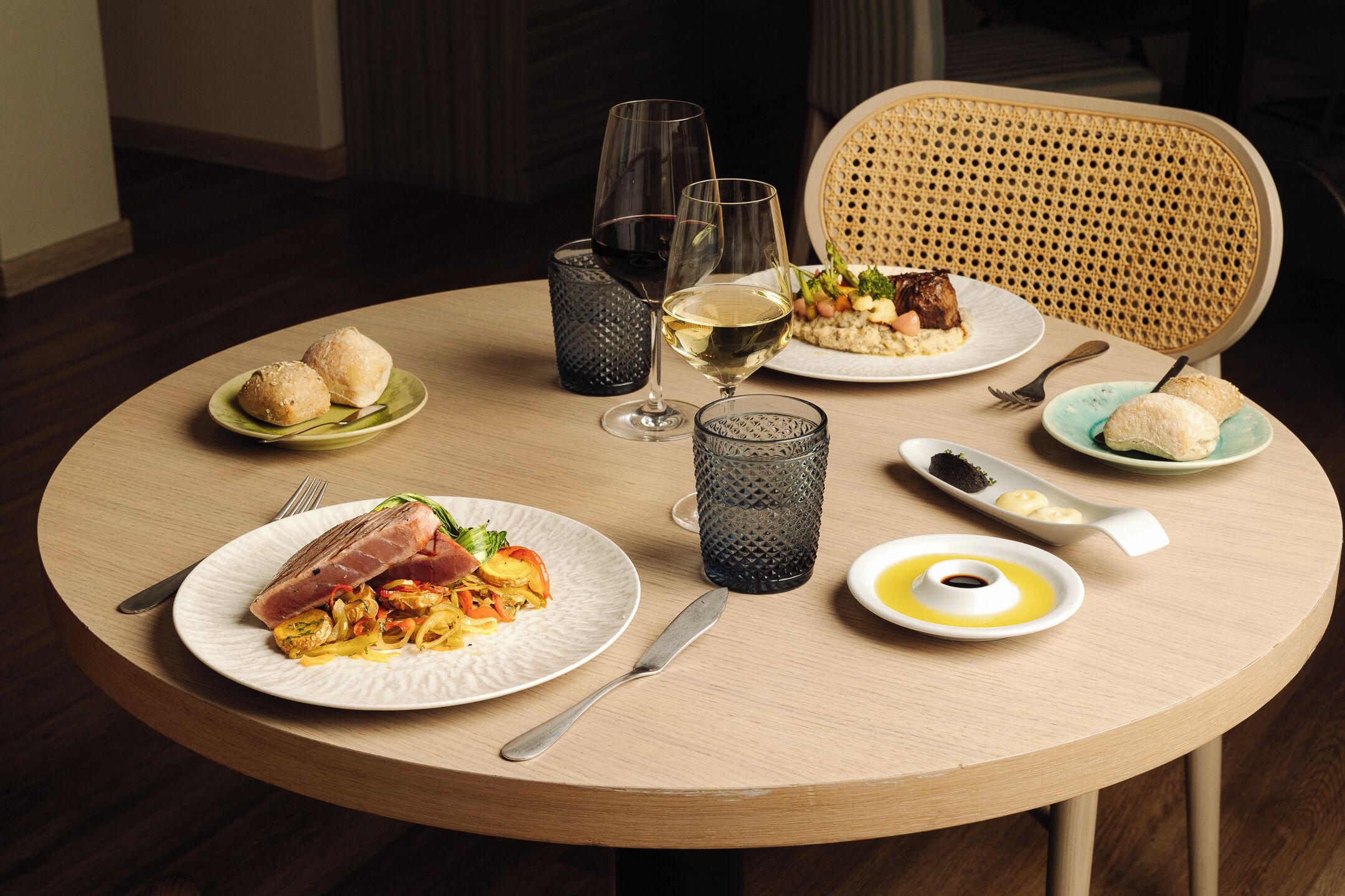 A round dining table with plates of food, glasses, and cutlery.