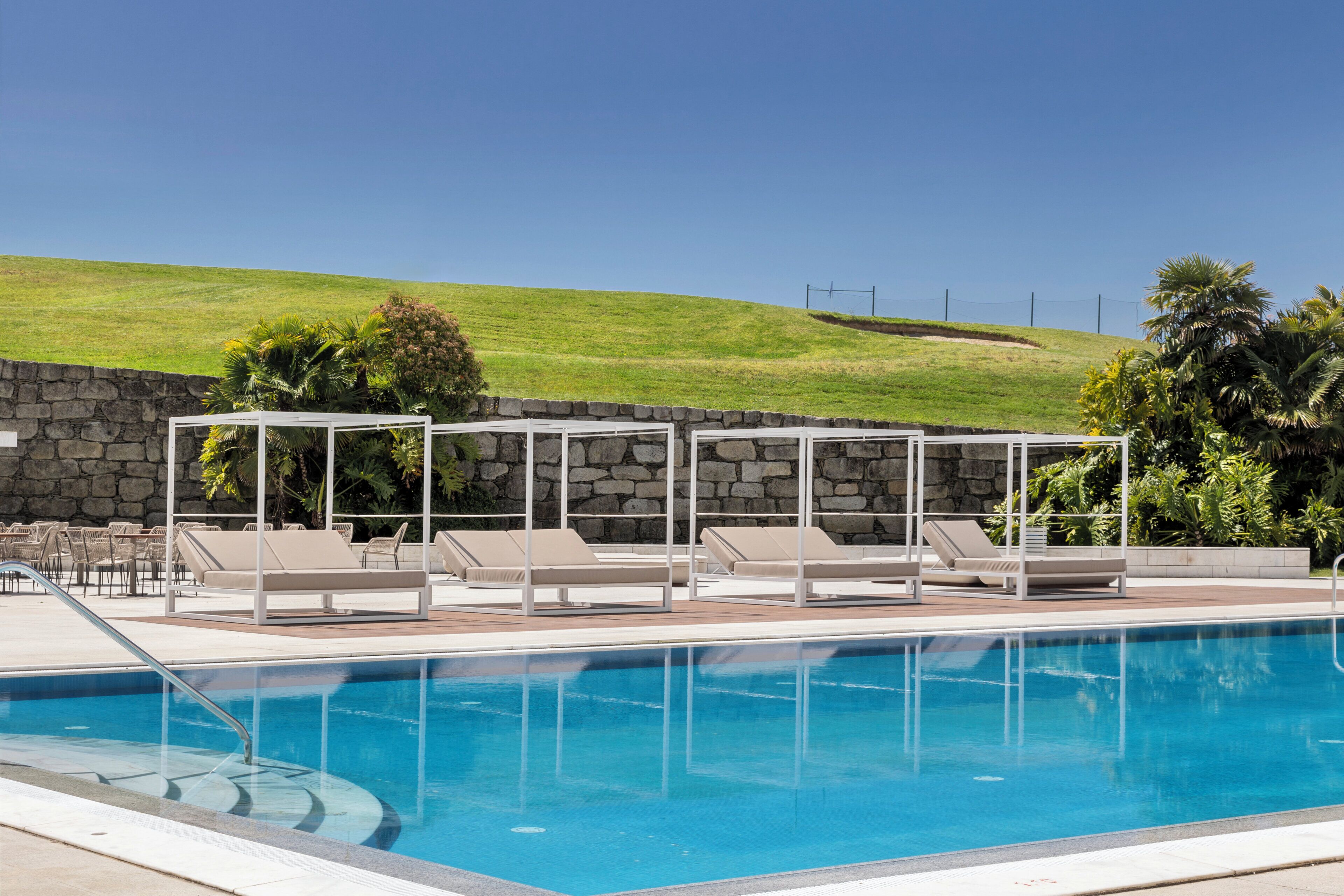 Una piscina con sillones de descanso y un muro de piedra.