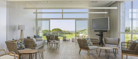 Amplia sala de estar con muebles de mimbre, un televisor de pantalla plana y grandes ventanales con vistas al exterior.