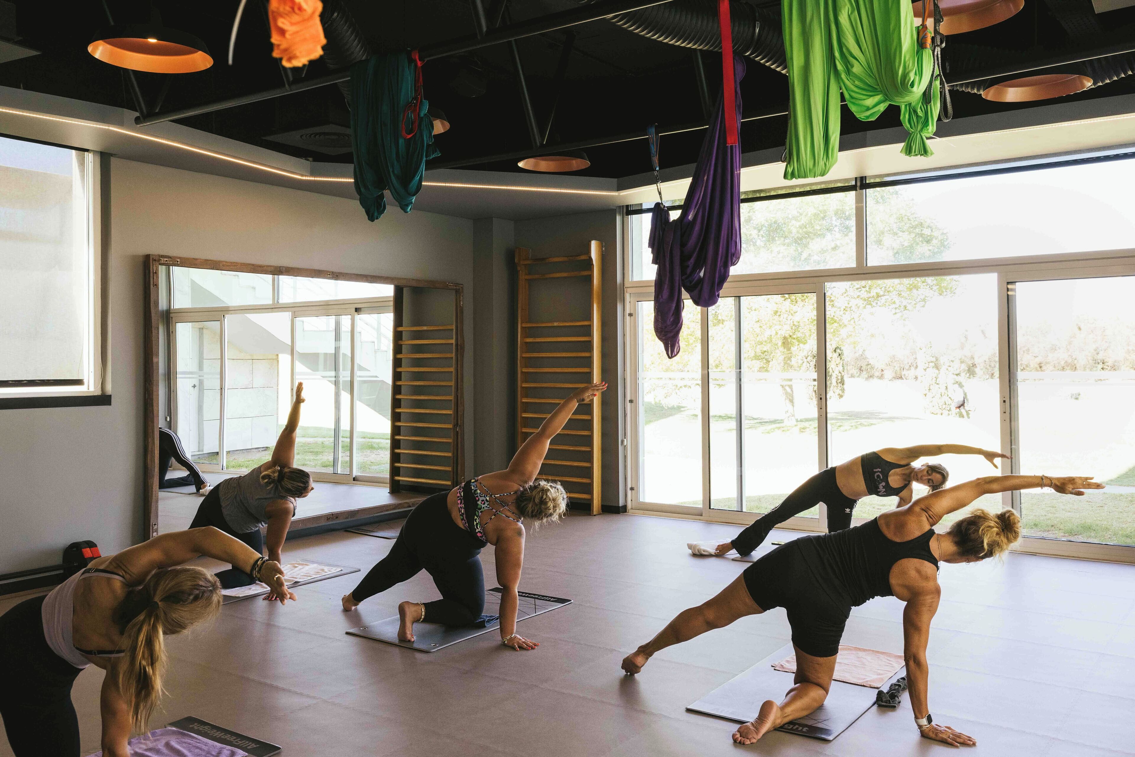 Un cours de yoga dans une pièce bien éclairée, dotée de grandes fenêtres et offrant une vue sur l’extérieur.