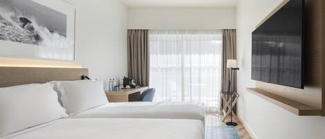 Habitación de hotel con una cama grande, un escritorio con silla, un televisor de pantalla plana montado en la pared y una ventana con cortinas.