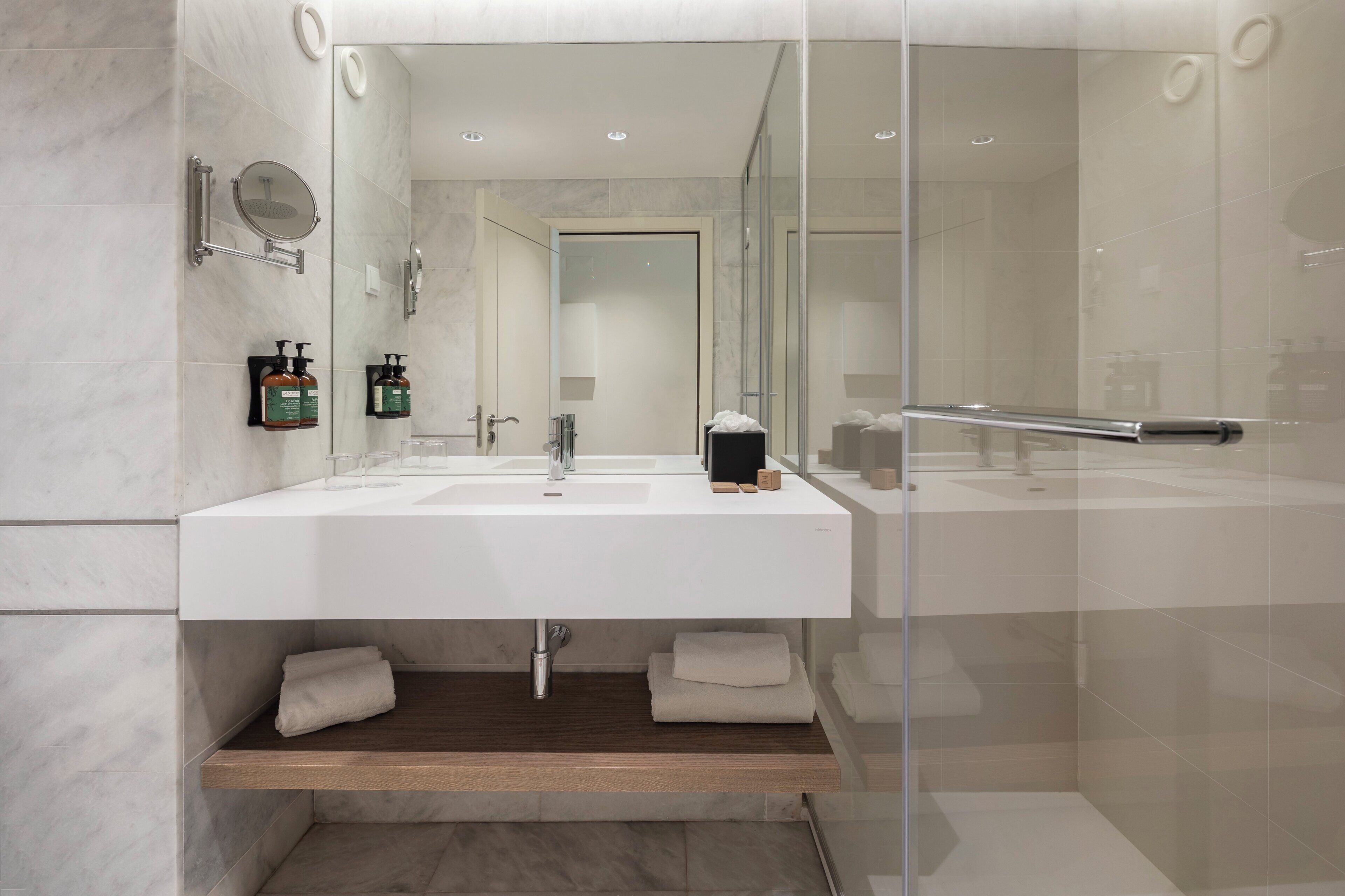 Un baño moderno con un espejo grande, dos lavabos y una ducha con mampara de vidrio.
