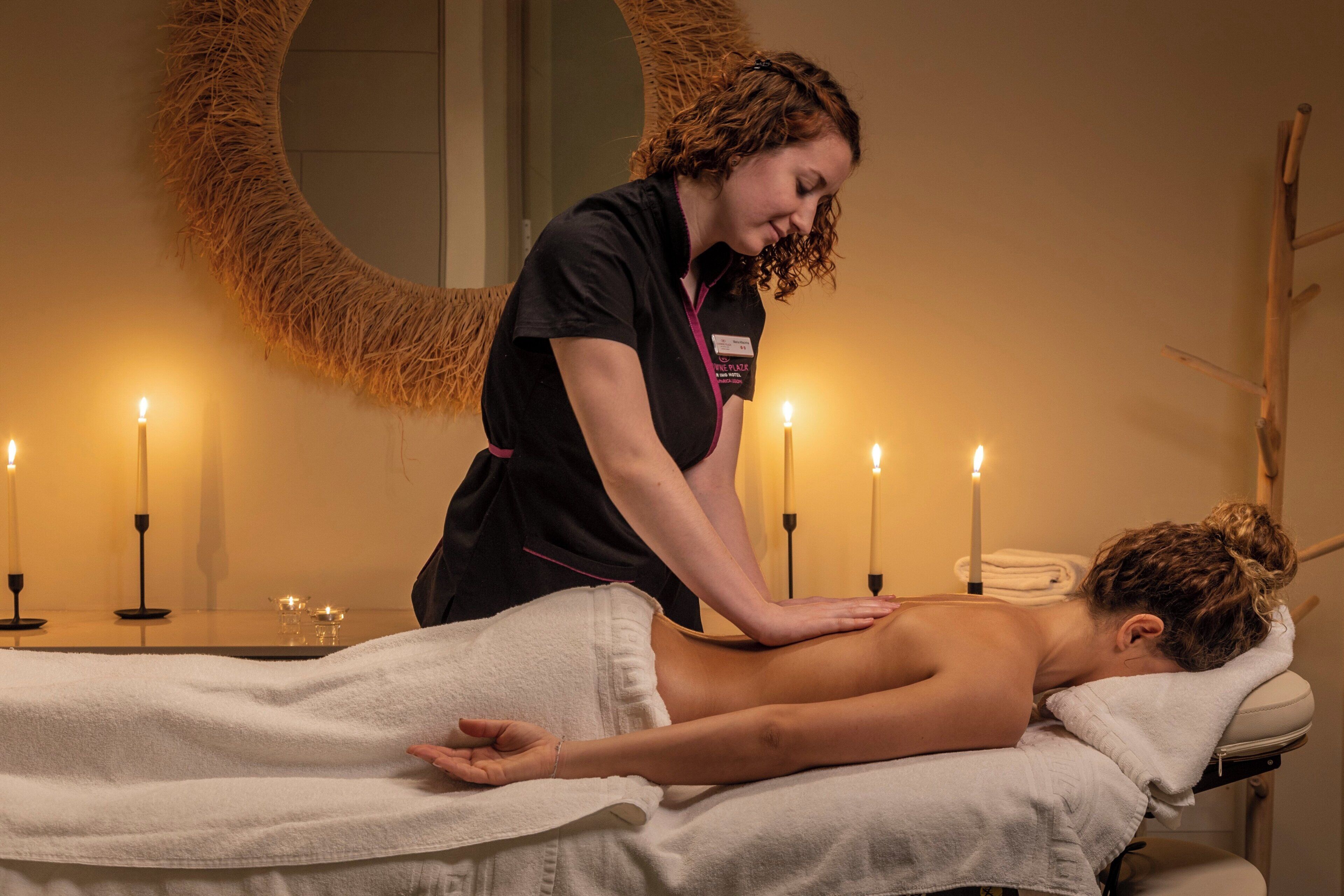 A massage therapy session in a room with a round mirror, candles, and a wooden chair.