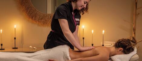 A massage therapy session in a room with a round mirror, candles, and a wooden chair.