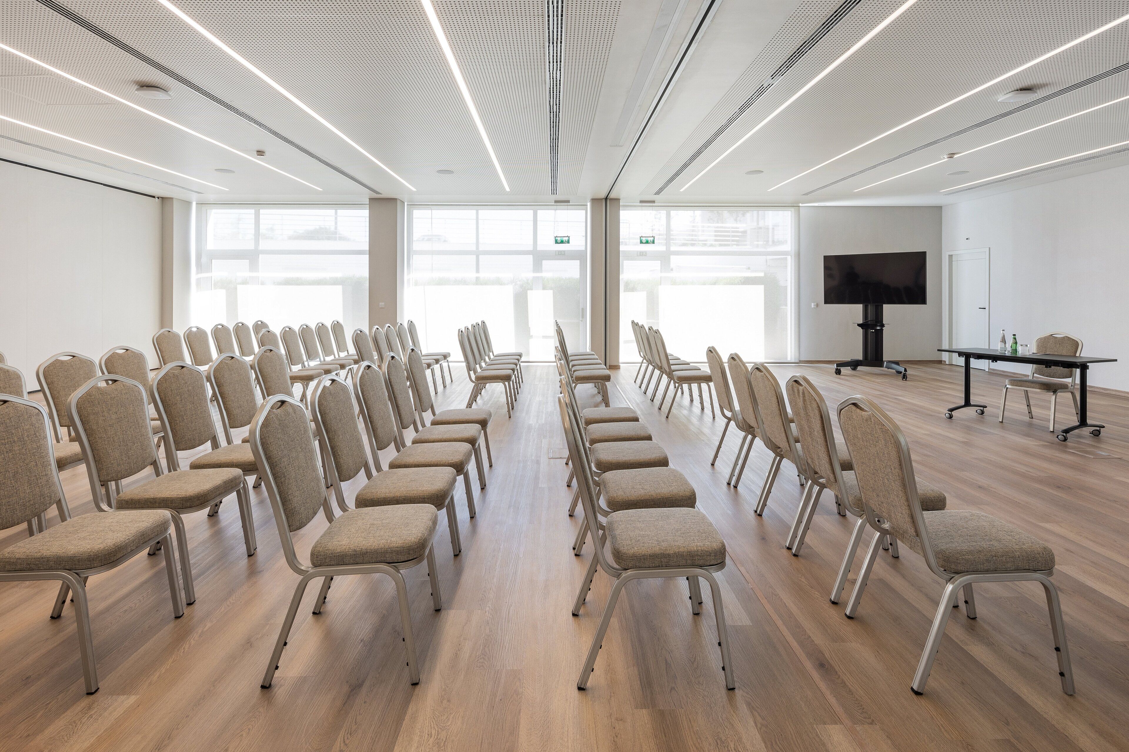 Un salón de conferencias con filas de sillas, una pantalla grande y una mesa con botellas.