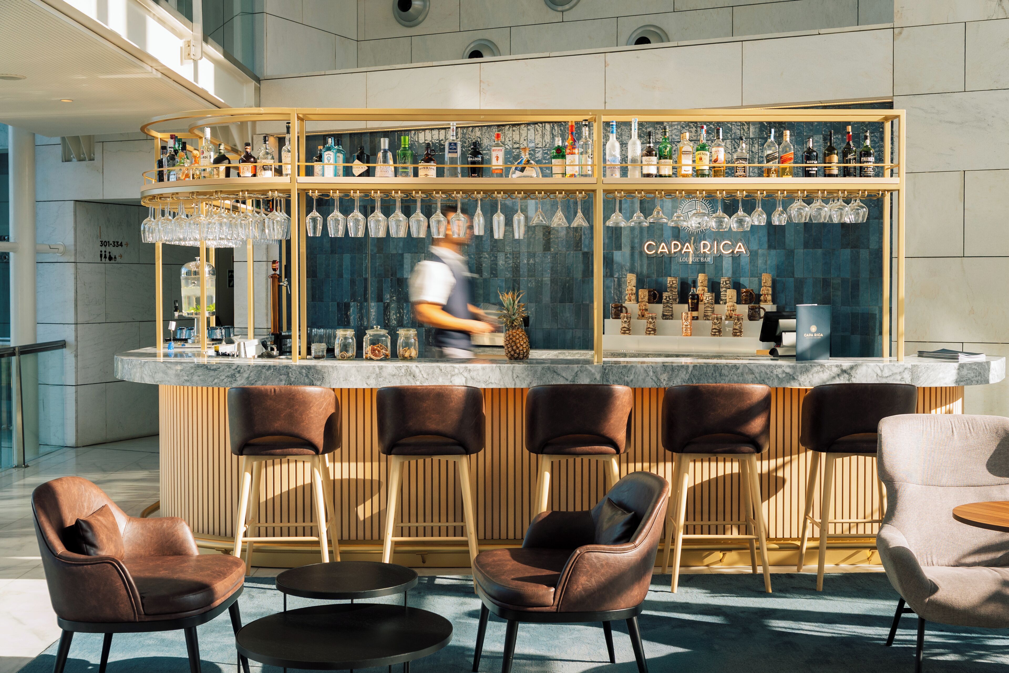 A bar area with a wooden counter, multiple stools, and a variety of bottles and glasses.