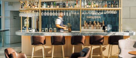 Una zona de bar con mostrador de madera, varios taburetes y una amplia selección de botellas y vasos.