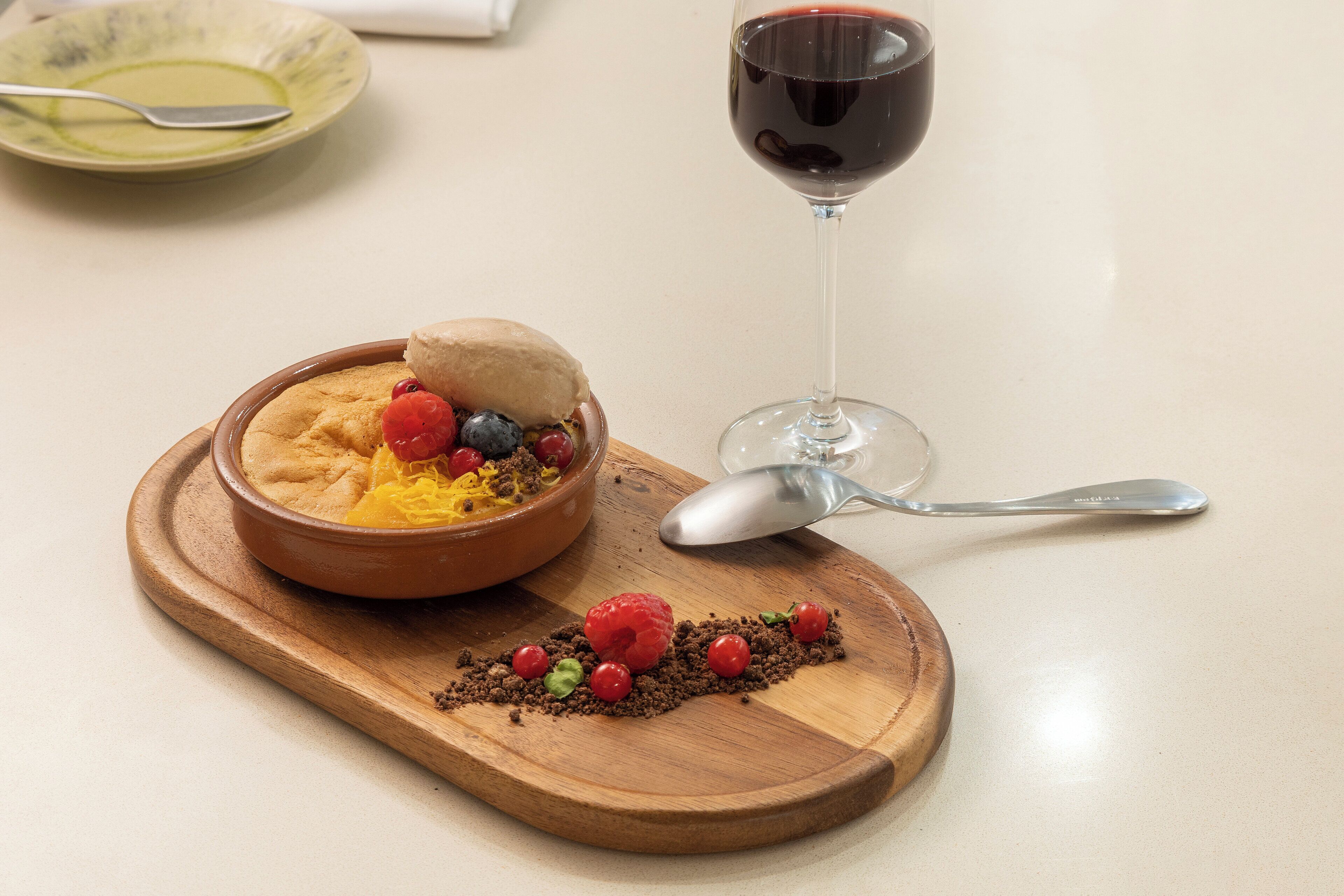 A dessert with berries and a glass of red wine on a wooden board.