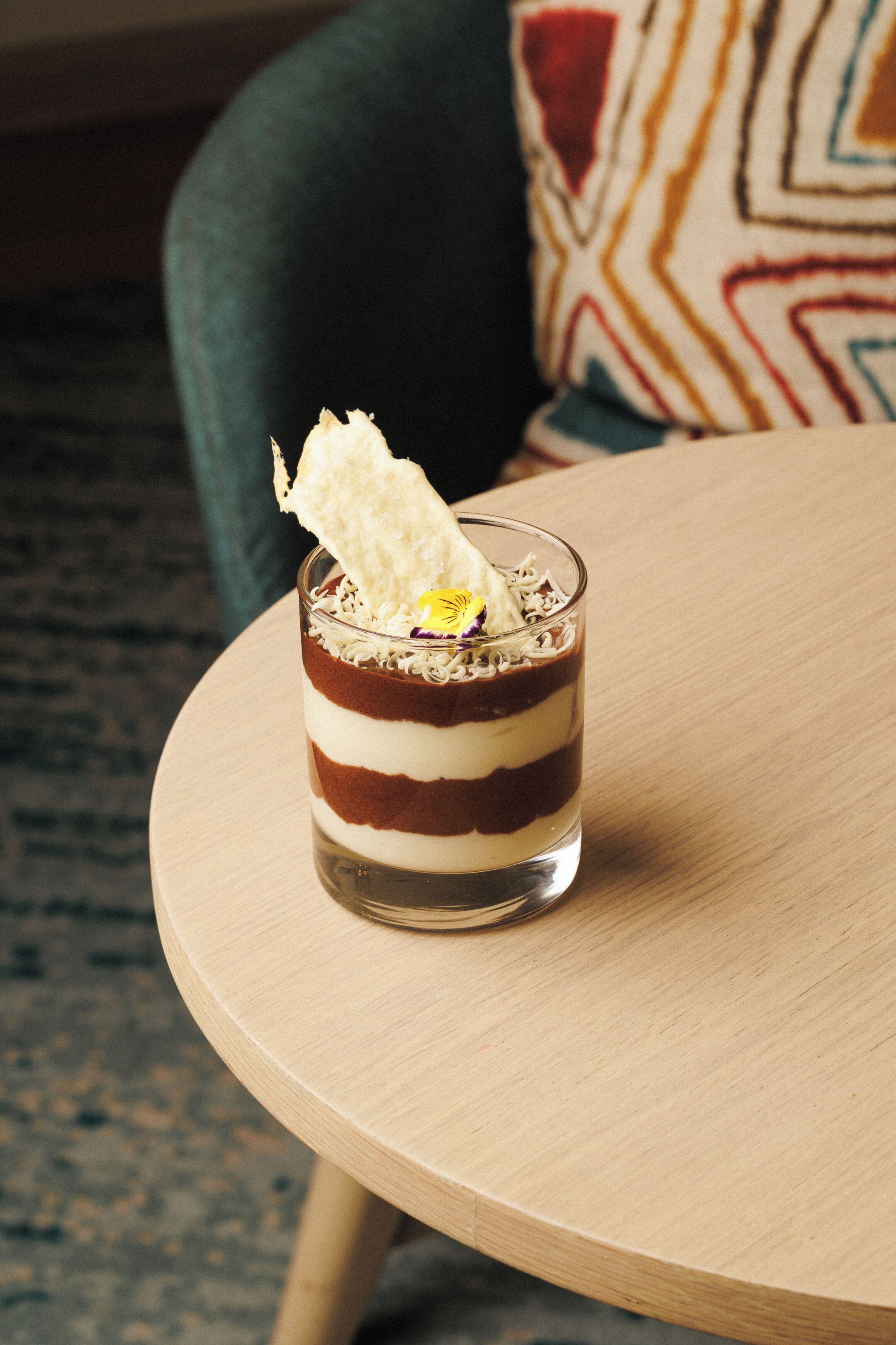 A dessert in a glass on a round wooden table.